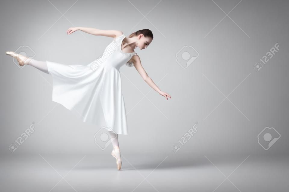 attractive young ballerina dancing in white dress on grey background