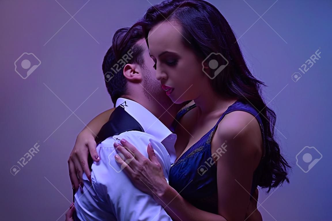 giovane uomo in camicia bianca che abbraccia e bacia una ragazza appassionata in lingerie nera su sfondo viola