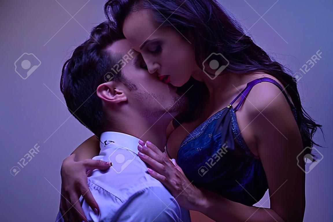 young man in white shirt hugging and kissing passionate girl in black lingerie on purple background