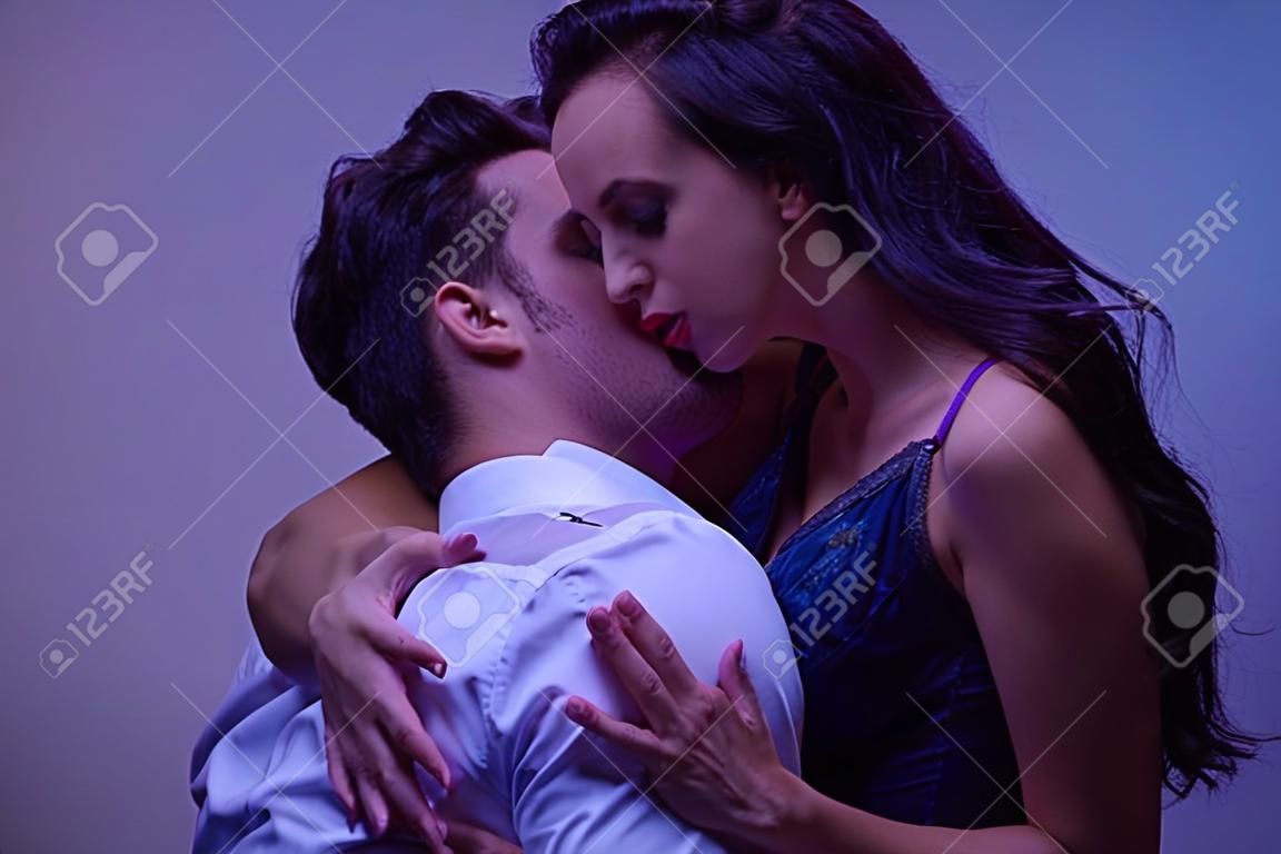 young man in white shirt hugging and kissing passionate girl in black lingerie on purple background
