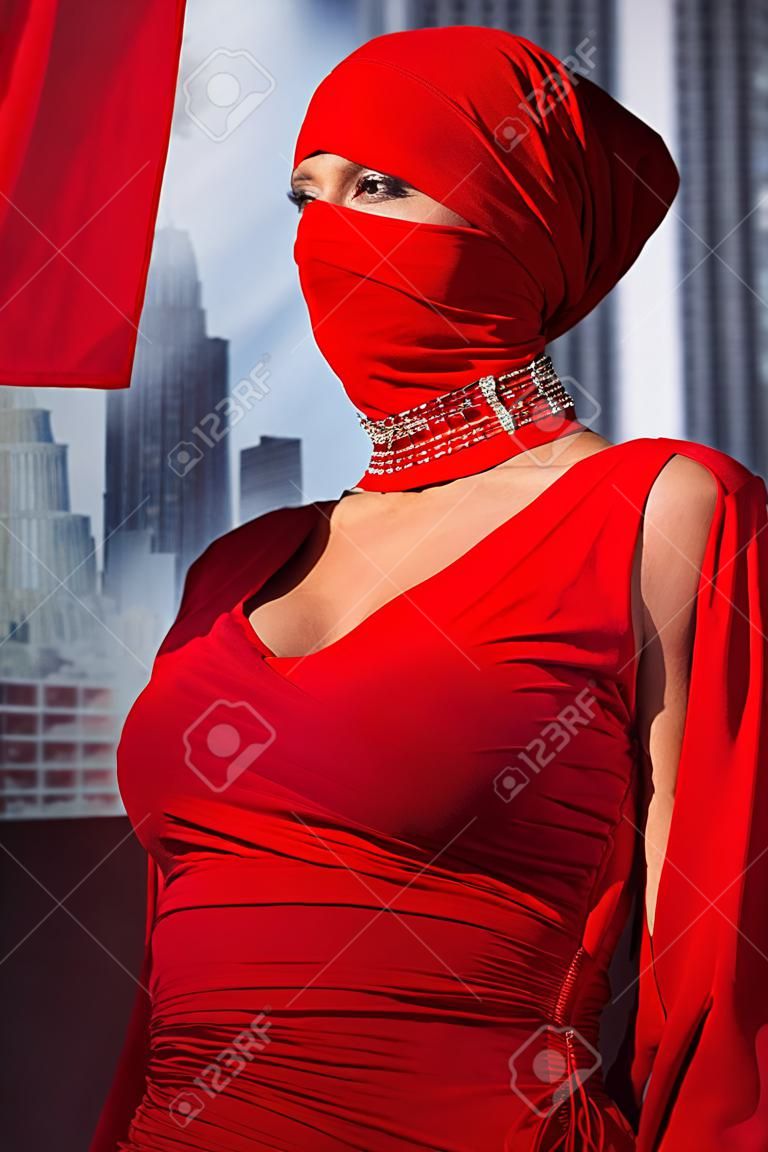 stylish woman in red dress and balaclava on city background 