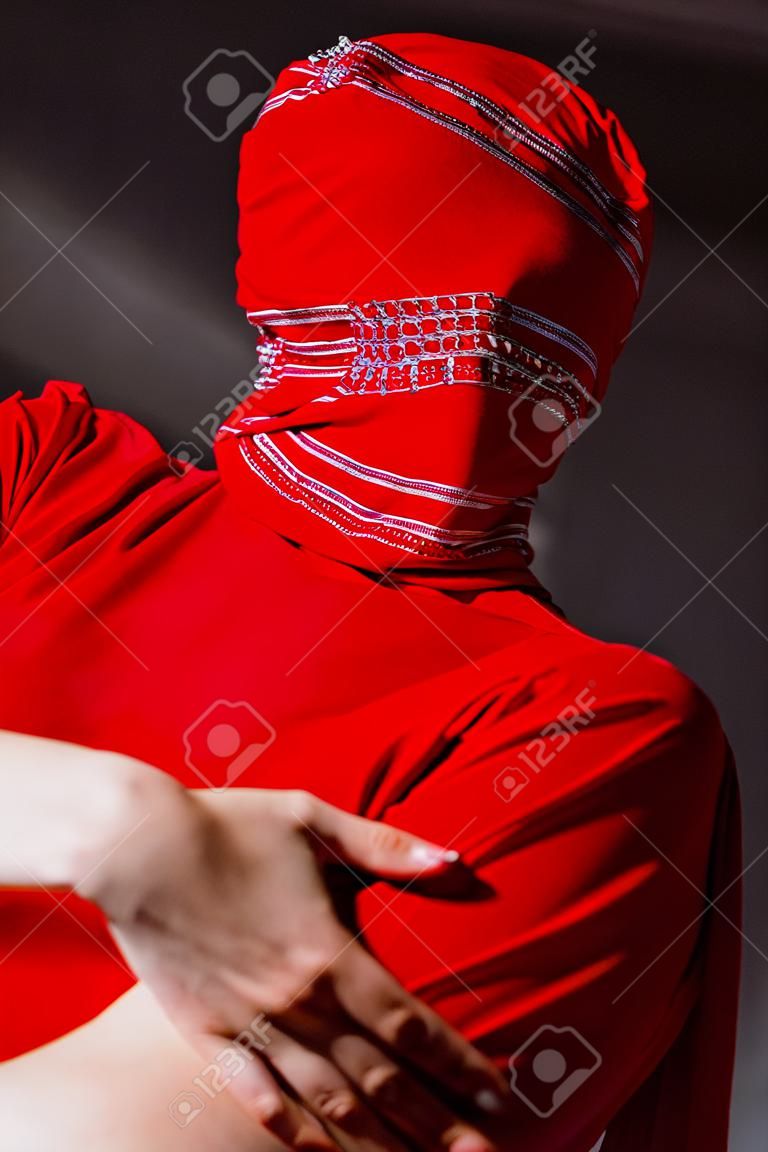 low angle view of stylish woman in red dress and balaclava isolated on grey