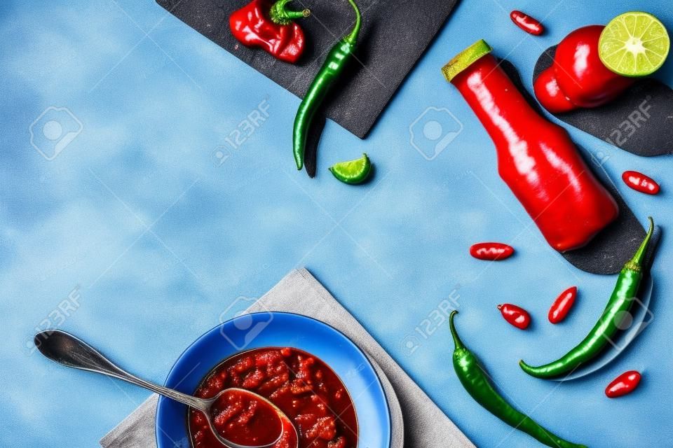 Top view of homemade chili sauce with garlic and chili pepper on blue surface