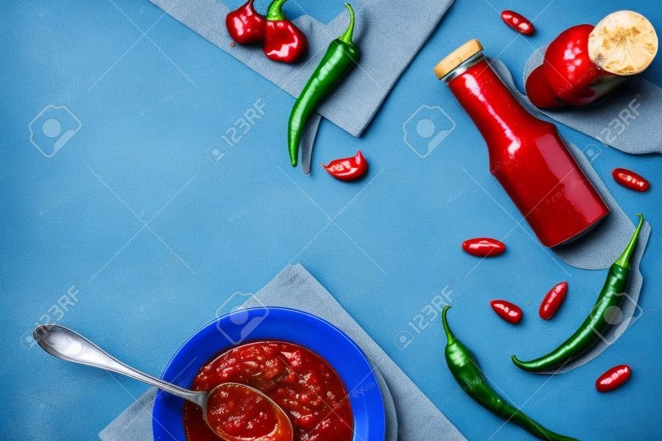 Top view of homemade chili sauce with garlic and chili pepper on blue surface