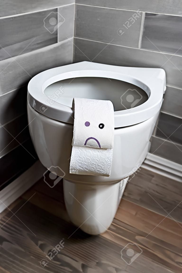 Sad emoticon on white toilet paper on toilet bowl in modern restroom