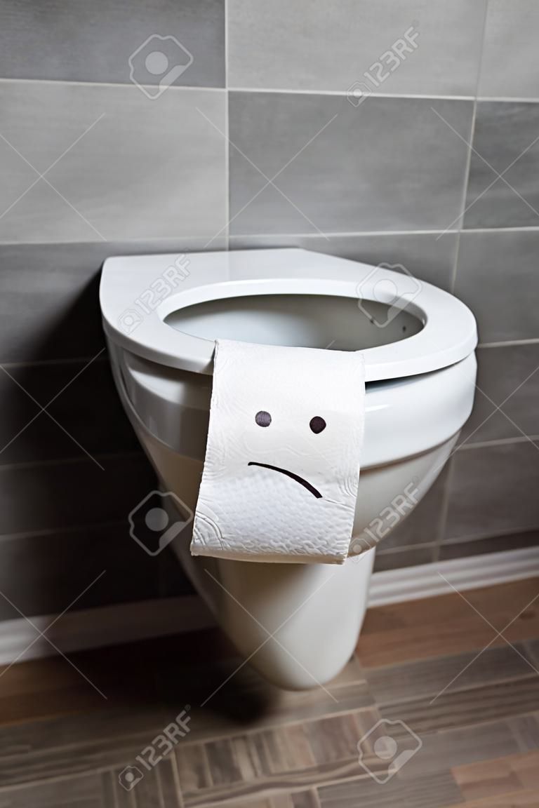 Sad emoticon on white toilet paper on toilet bowl in modern restroom
