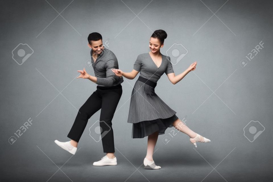 junge Tänzer, die Händchen halten, während sie Boogie-Woogie auf grauem Hintergrund tanzen