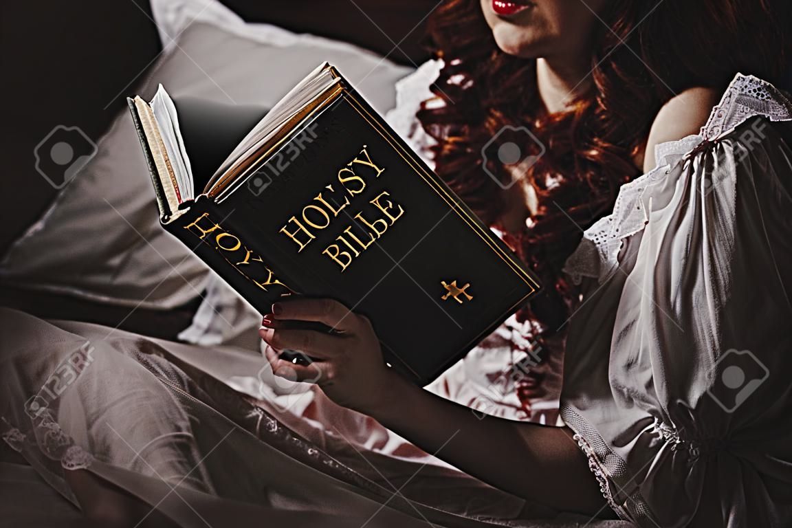 vista recortada del demonio femenino en camisón leyendo la sagrada biblia en la cama