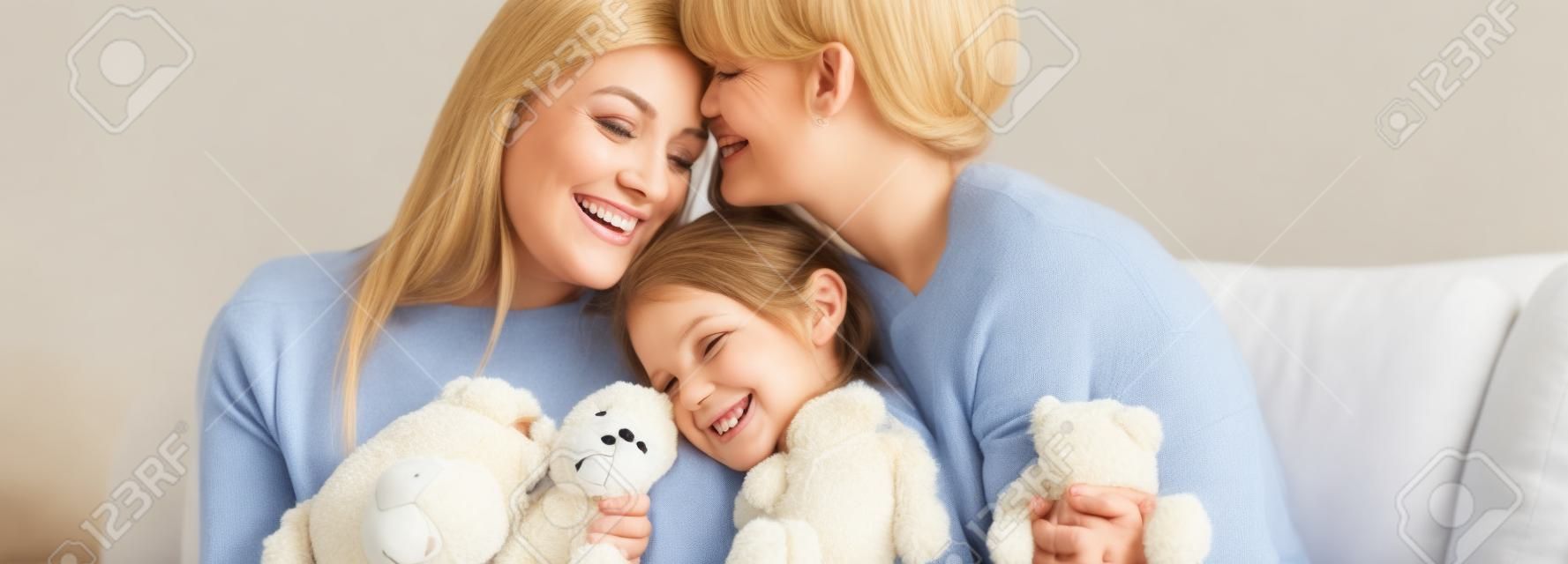 Gelukkige moeders omhelzen glimlachende dochter met teddybeer op de bank, panoramisch schot