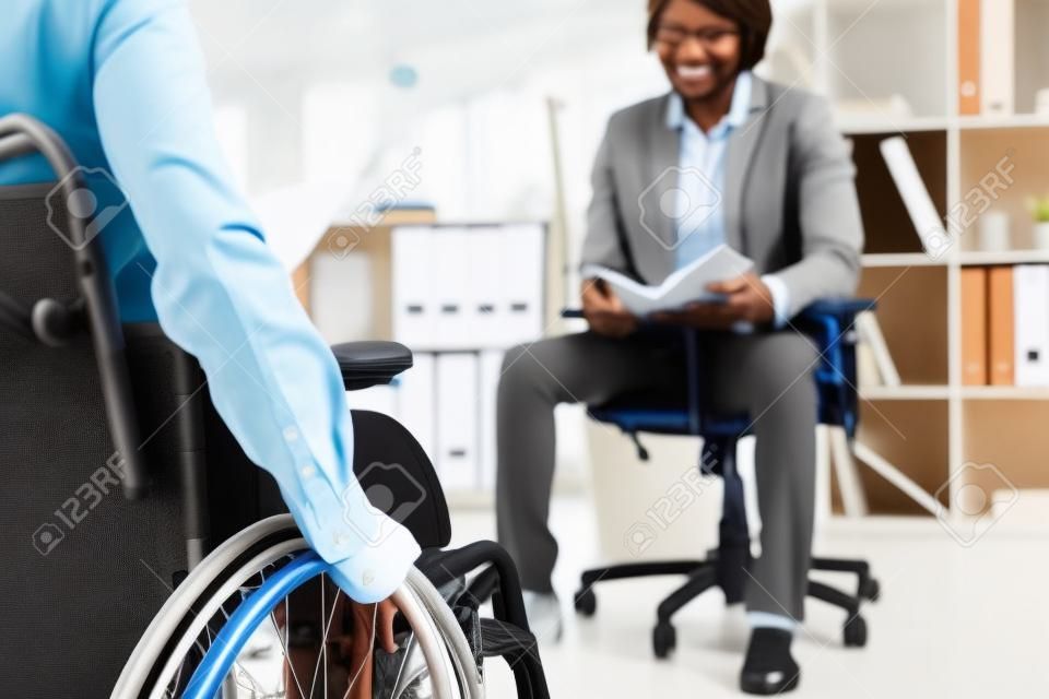 Cropped view of disabled recruiter on wheelchair and african american employee with notebook in office