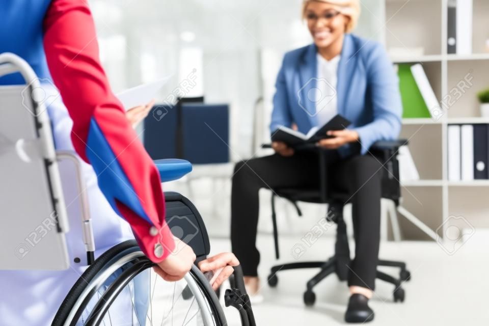 Cropped view of disabled recruiter on wheelchair and african american employee with notebook in office