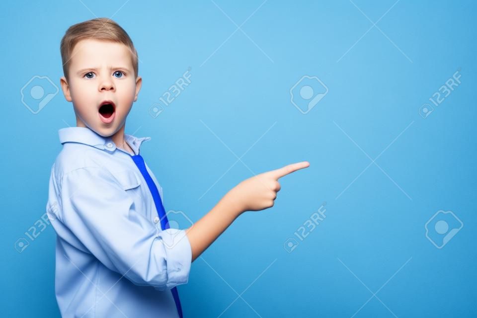 shocked and cute kid pointing with finger on blue background