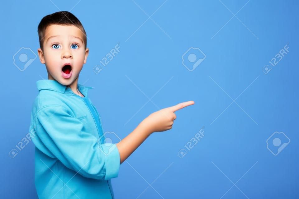 shocked and cute kid pointing with finger on blue background