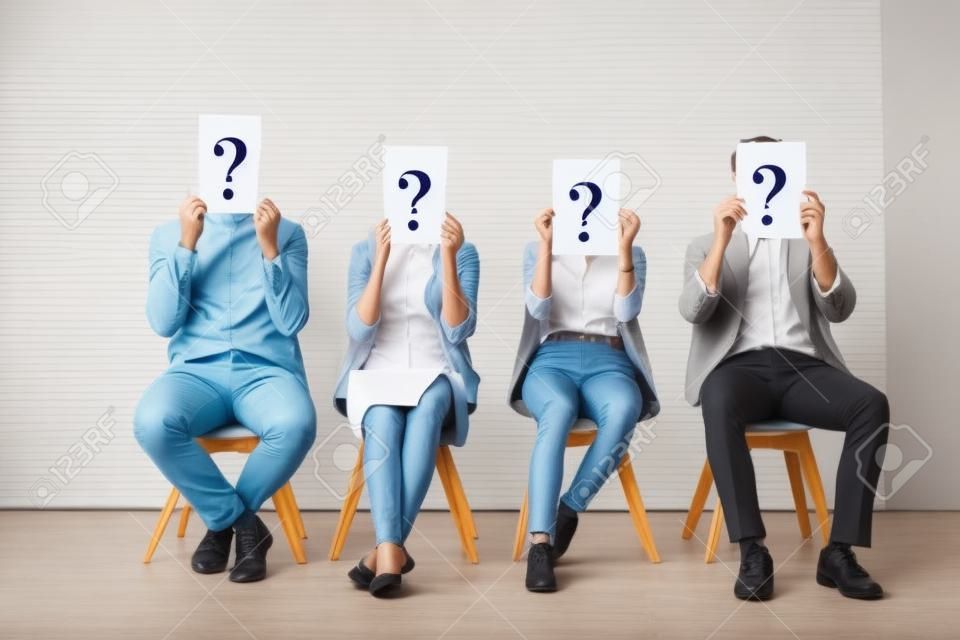 Young people holding cards with question marks while waiting for job interview in office