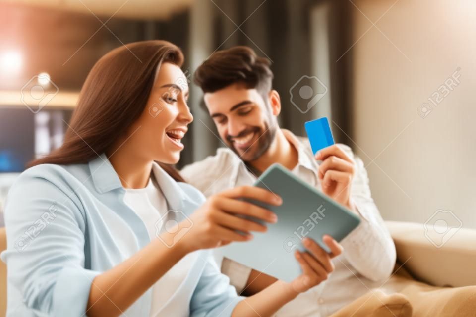 Selective focus of man holding credit card near excited girlfriend showing digital tablet at home