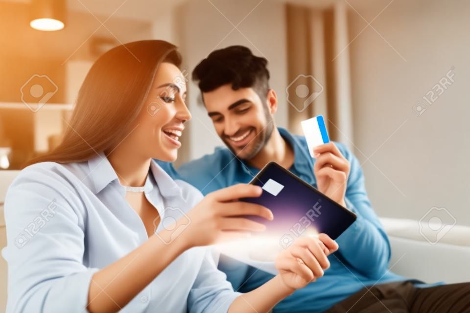 Selective focus of man holding credit card near excited girlfriend showing digital tablet at home