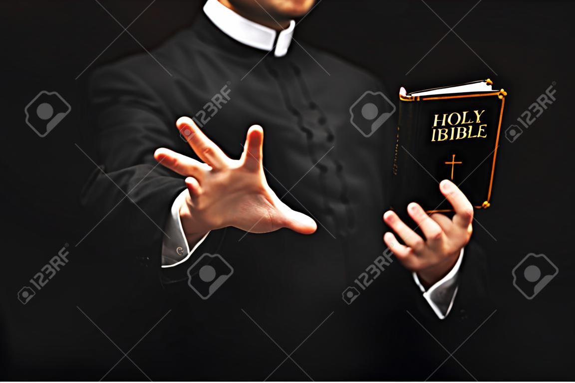 bijgesneden uitzicht van priester houden heilige bijbel tijdens gesturderen geïsoleerd op zwart