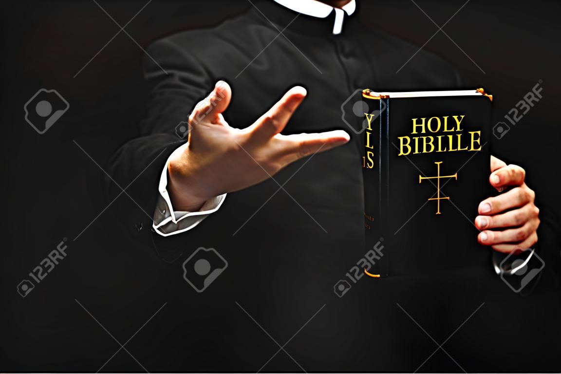 vista ritagliata del sacerdote che tiene la Sacra Bibbia mentre gesticola isolato sul nero