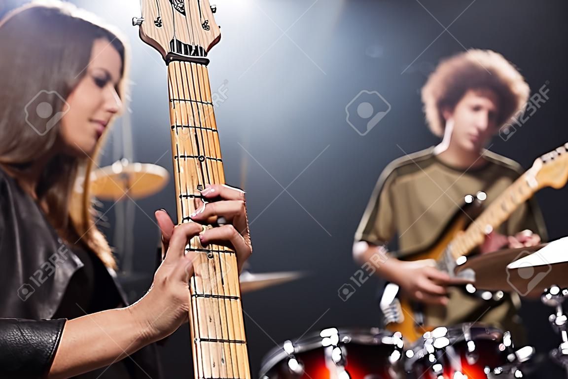 Vista de cima do músico fêmea que joga a guitarra elétrica com o baterista e o kit borrados da bateria no fundo