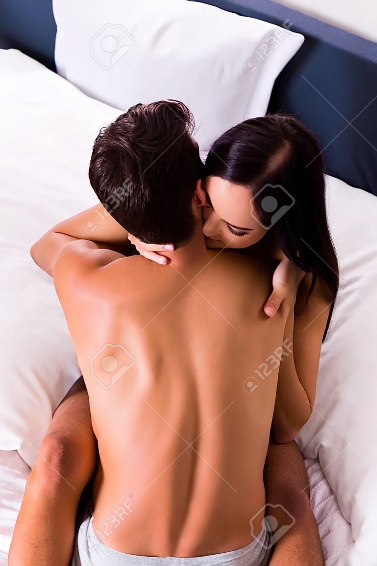 high angle view of smiling brunette woman hugging shirtless man on bed