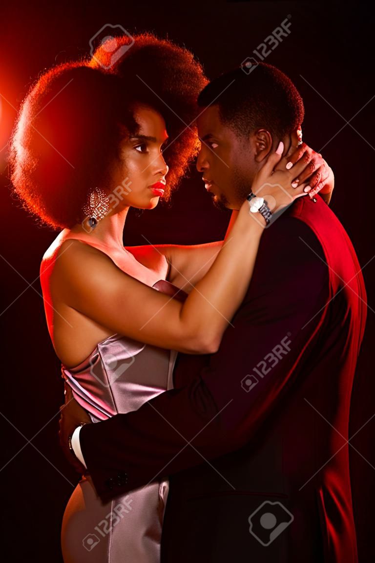 elegant african american woman in dress embracing man on black