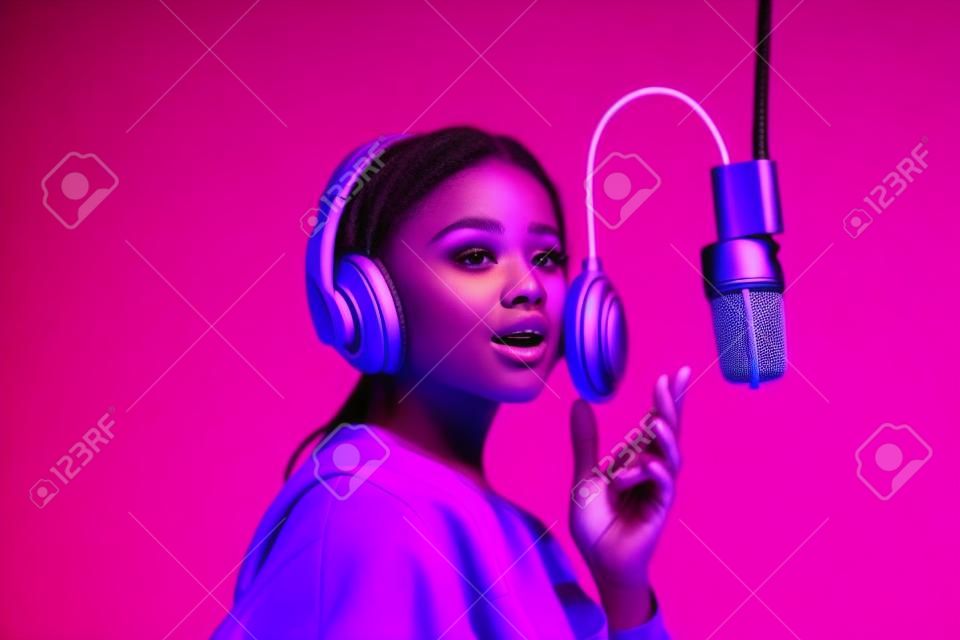 young singer in wireless headphones singing song in microphone on purple
