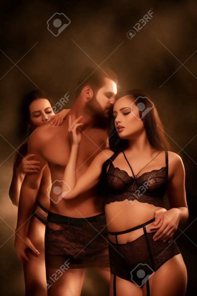 passionate women in lingerie seducing shirtless man isolated on black