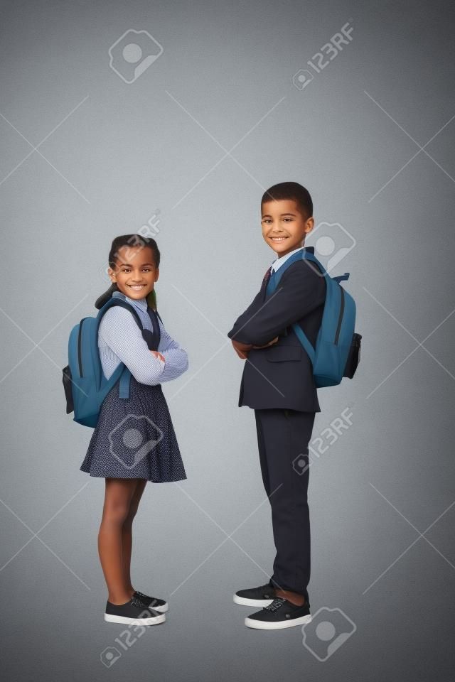 écoliers avec sacs à dos posant avec les bras croisés sur gris