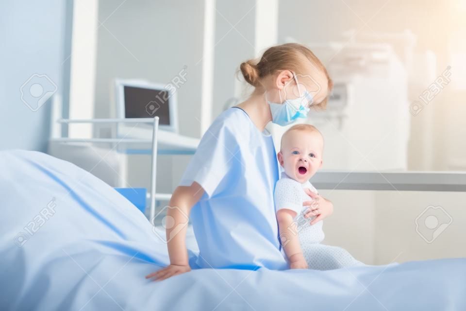 Niña con la boca abierta mirando hacia otro lado cerca de la madre en bata de paciente sentada en la cama del hospital