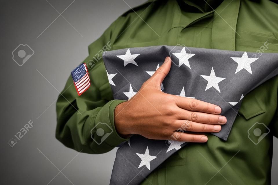 회색에 고립 된 현충일 동안 미국의 접힌 국기를 들고 미국 군인의 부분 보기