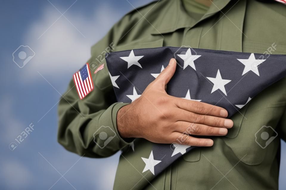 회색에 고립 된 현충일 동안 미국의 접힌 국기를 들고 미국 군인의 부분 보기