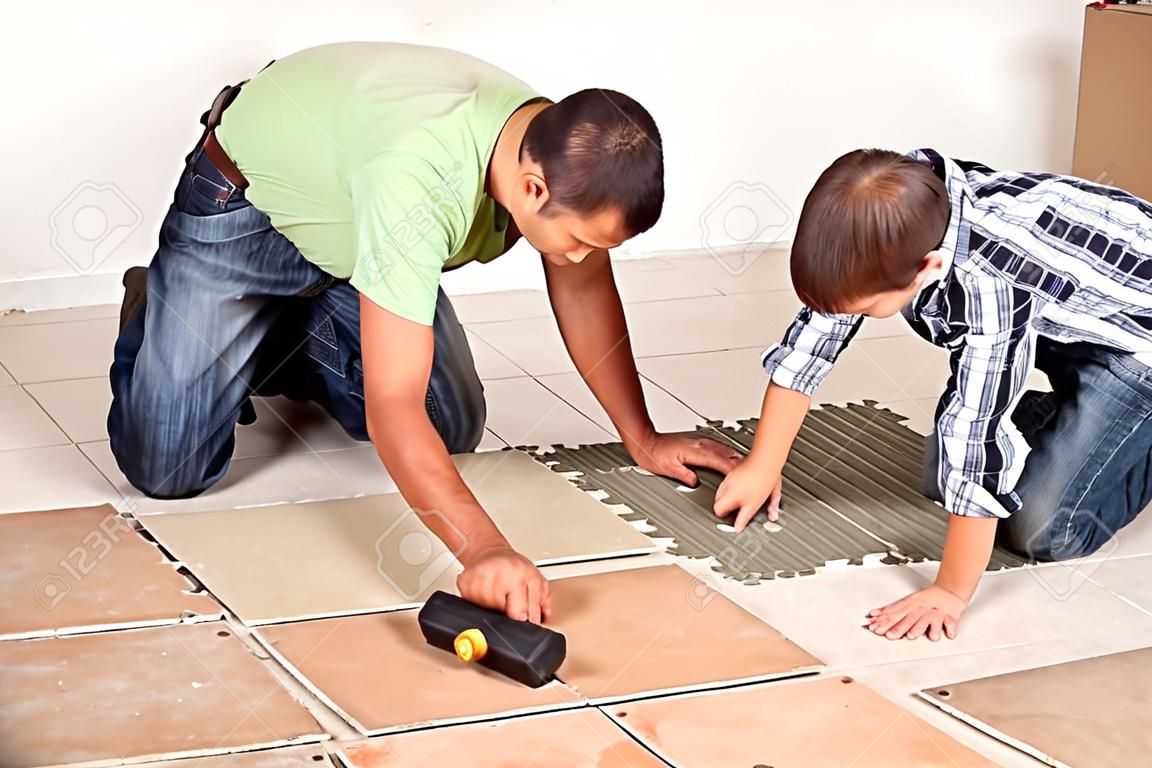 Man laying ceramic floor tiles helped by his son to evenly space the pieces