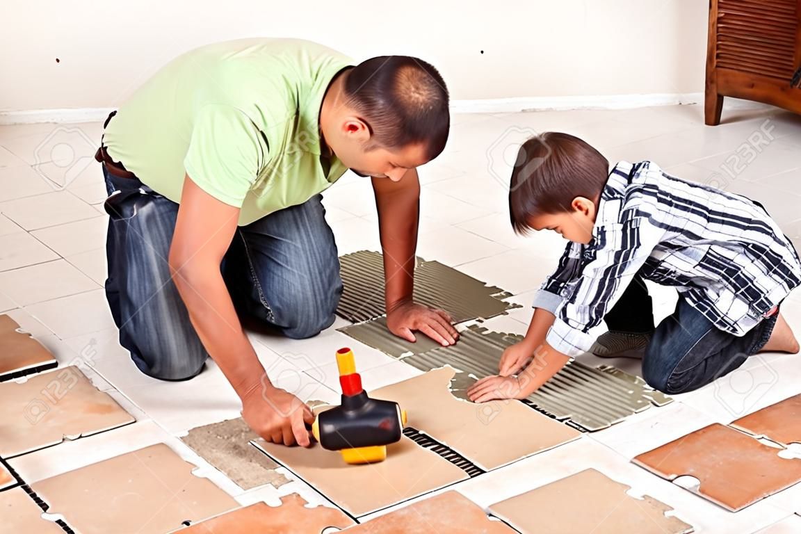 Man laying ceramic floor tiles helped by his son to evenly space the pieces