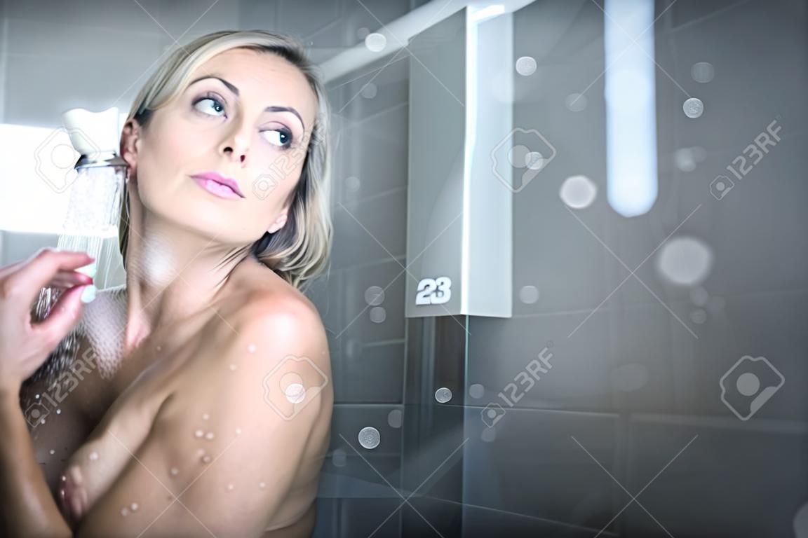 Mujer tomando una larga ducha caliente lavándose el pelo en un baño de diseño moderno
