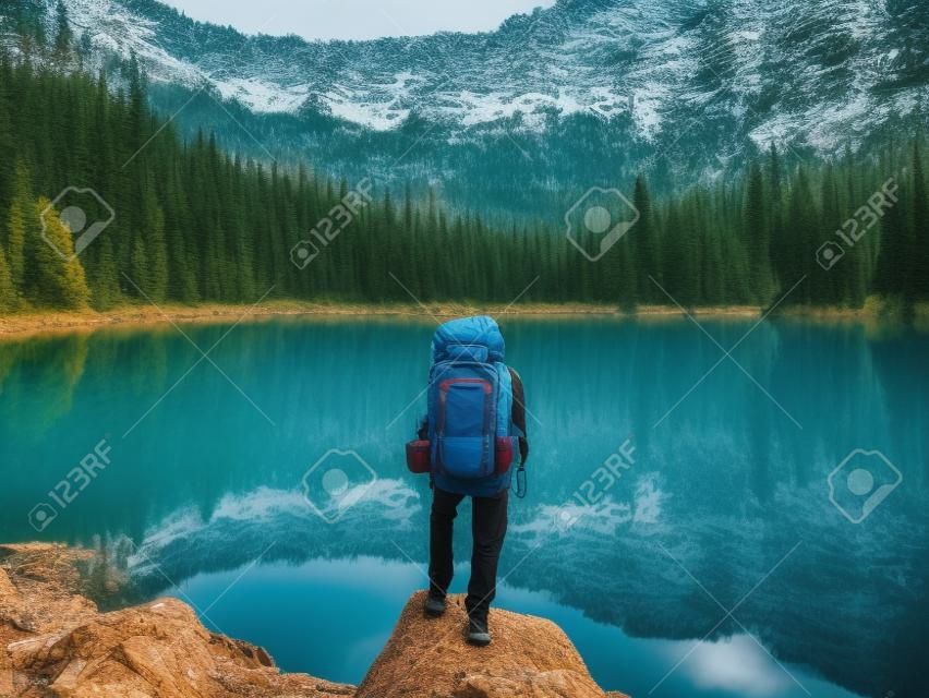 Turista activo con mochila de pie en el lago de montaña y fondo de madera de pino
