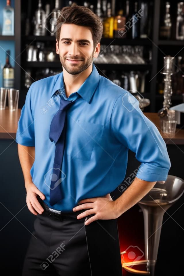 Retrato de apuesto barman, de pie delante de la barra de