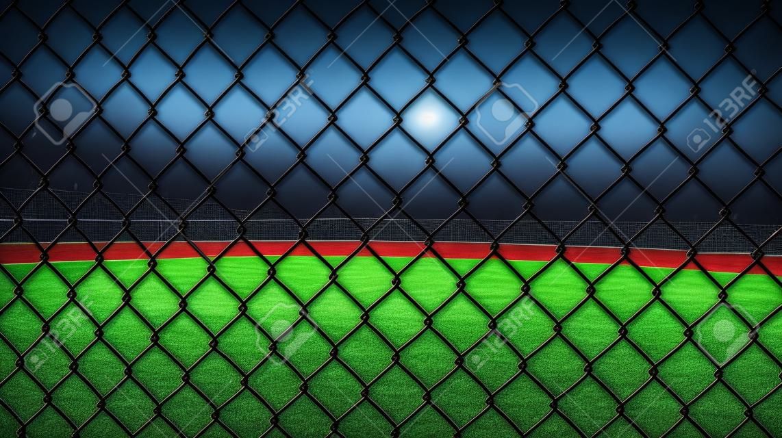 野球場のフェンスの写真を夜に空のフィールドに見て閉じます。バックグラウンドでの使用に最適です。