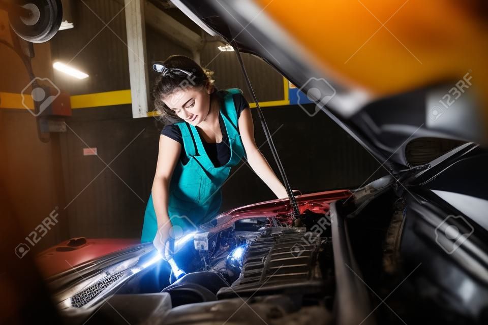 Mechanic woman repairing motor or electric parts of car in garage. Beautiful lady working at service station.