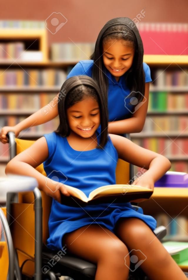 Two school girls reading notes in the library.  One is in a wheelchair.  