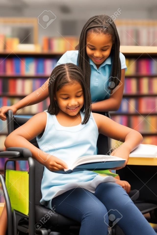 Two school girls reading notes in the library.  One is in a wheelchair.  