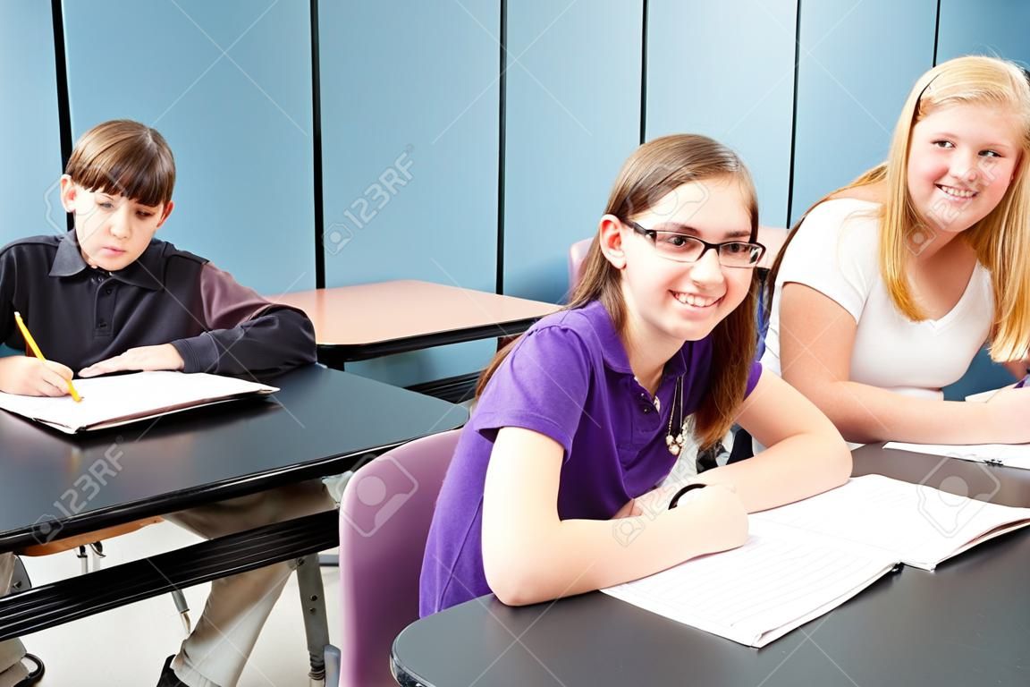 Hat serdülő iskolás gyerekek ülnek az asztaloknál az osztályban.