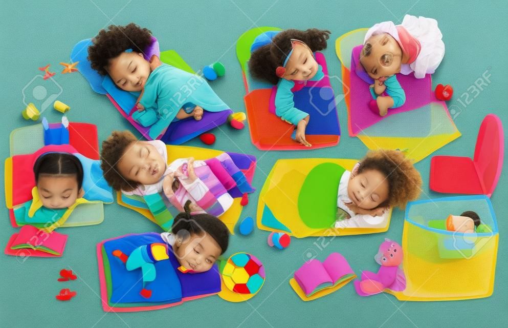 Nap time in the kindergarten. Group of multiracial girls and boys have a nip time at a colorfill nap mats. Preschool dream time. Two girls gossip during daytime sleep.