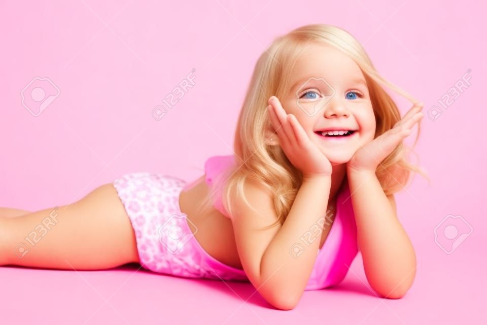 petite fille heureuse blonde en maillot de bain rose sur fond blanc couché sur le plancher