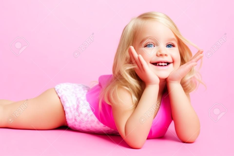 petite fille heureuse blonde en maillot de bain rose sur fond blanc couché sur le plancher