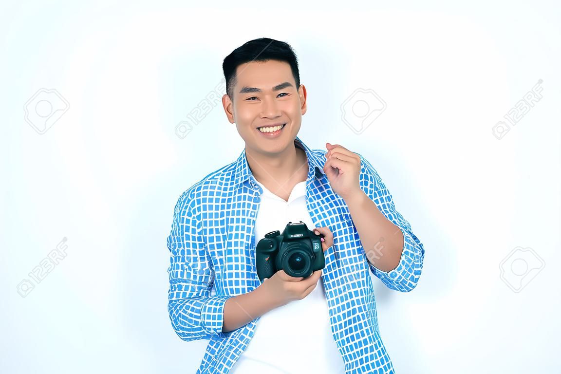 Homem asiático feliz que prende a câmera e que sorri na câmera contra o fundo branco