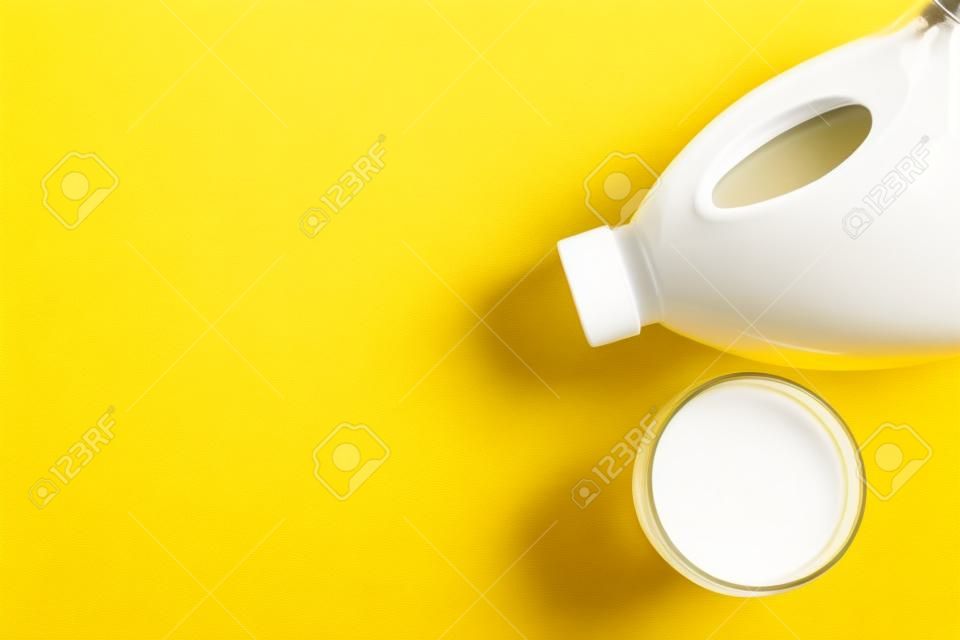 Gallon bottle and glass of milk on yellow background, flat lay. Space for text