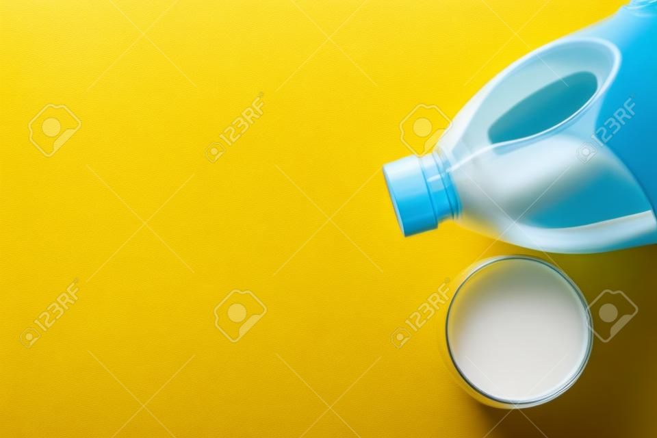 Gallon bottle and glass of milk on yellow background, flat lay. Space for text