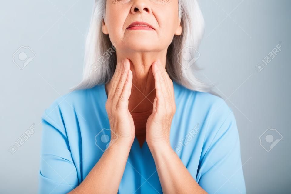 Mature woman doing thyroid self examination on light background, closeup