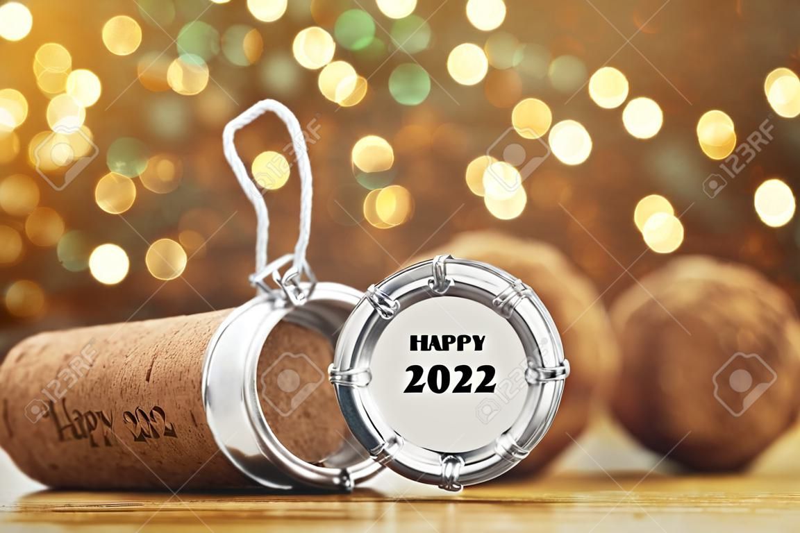Cork of sparkling wine and muselet cap with engraving Happy 2023 New Year on wooden table against blurred festive lights, space for text. bokeh effect