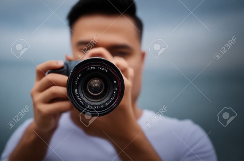 Photographer taking picture with professional camera outdoors, focus on lens